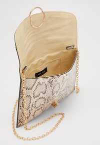 Pieni olkalaukku, jossa on beige käärmeennahkakuosi, kultaketju olkahihna, beige kangasvuori ja "New Look" -etiketti sisällä.