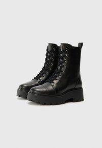 Bottes noires en cuir lacées avec un bout arrondi, une semelle plateforme chunky et des œillets en métal, dotées d'une languette à l'arrière et d'une texture lisse.
