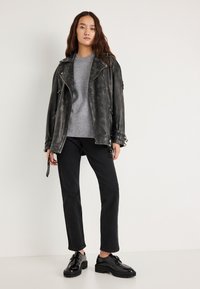 Melnas ādas motociklista jaka ar sudraba rāvējslēdzējiem, pelēks trikotāžas džemperis, melnas taisnas bikses un spīdīgas melnas mežģīņu kurpes.