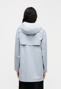 Svetlomodrá nepremokavá bunda s kapucňou, dlhými rukávmi a voľným strihom. Má zadný panel na vetranie a hladkú textúru.