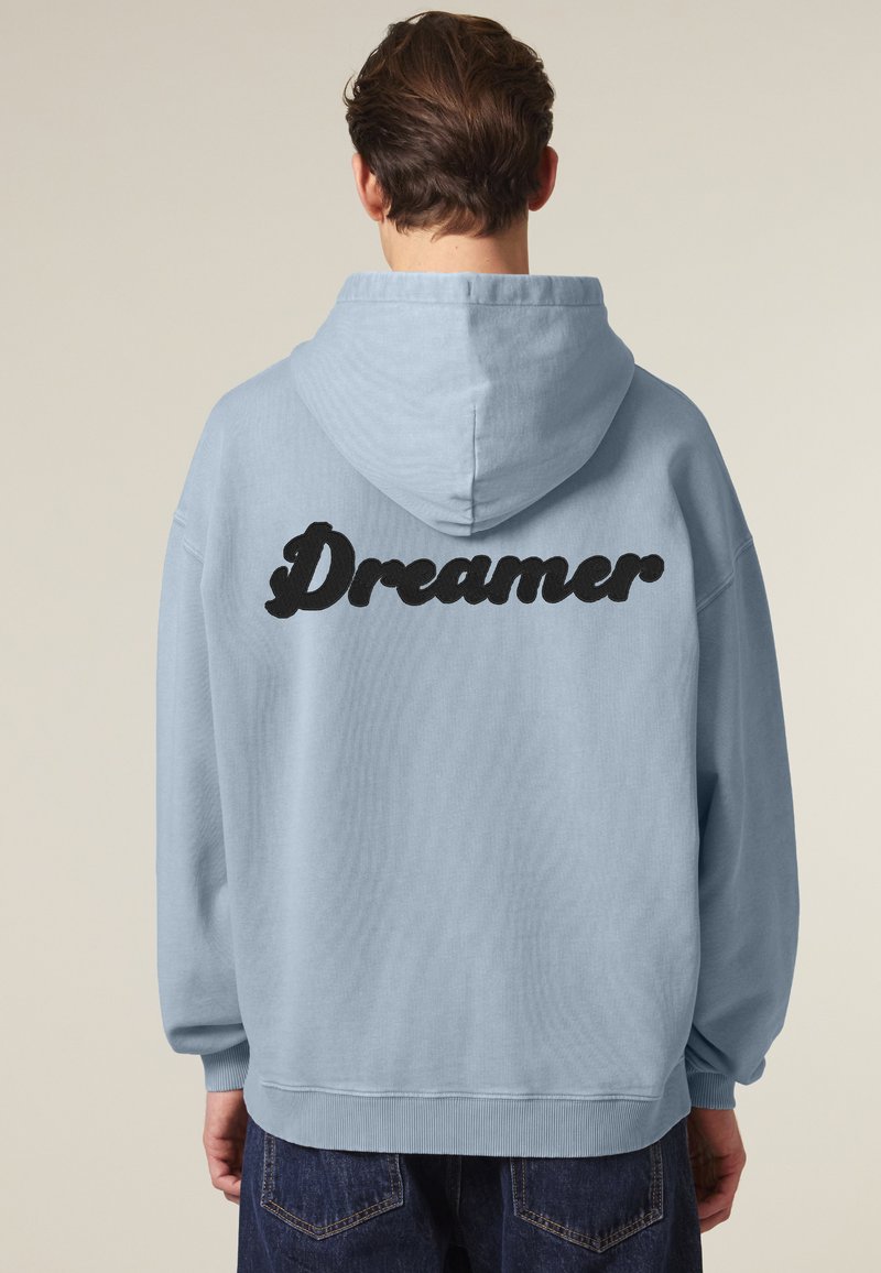 Felpa blu chiaro con una grande stampa nera "Dreamer" sul retro. Caratterizzata da una vestibilità comoda, maniche lunghe e cappuccio con cordino.