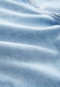 Helehall sinine teksariidest kangas, millel on sile tekstuur, peen diagonaalne koepattern ja oranž õmbluse detail, mis on pehmetes voldikutes laotud.