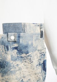 Chaqueta de mezclilla con mangas de algodón blanco, que presenta un bolsillo texturizado en azul y crema, detalles de botones y una mezcla de tejidos suaves y ásperos.