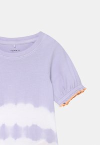 T-shirt lil�ás com nervuras e mangas curtas bufantes, apresentando um acabamento com franja laranja e um padrão de tie-dye em branco na metade inferior.