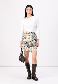 Top alb cu mâneci lungi, combinat cu o fustă în mai multe straturi, cu un imprimeu animalier texturat. Botine maronii până la genunchi și o geantă mică completează look-ul.