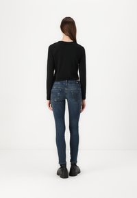 Black long-sleeve top paired with dark blue skinny jeans featuring a slight fade and back pocket embellishments, worn with black chunky shoes.