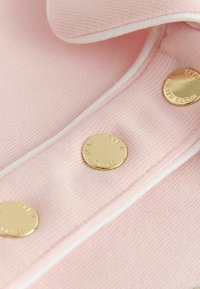 Weicher rosa Strickstoff mit weißem Besatz und glänzenden goldenen runden Knöpfen, graviert mit der Aufschrift "TED BAKER".