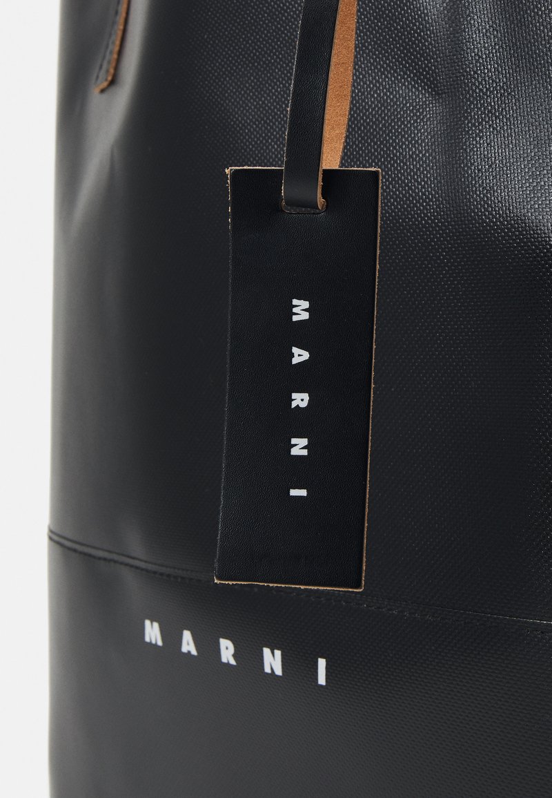 Sac fourre-tout noir avec une finition texturée, doté d'une étiquette en cuir portant l'inscription "MARNI" en blanc, et d'accents en cuir marron clair contrastants.