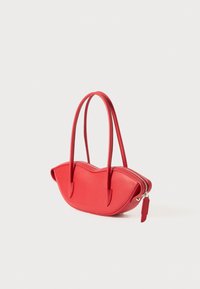 Sac à main rouge en cuir lisse avec un design incurvé et festonné, deux poignées et une fermeture éclair. Il comporte une petite étiquette décorative.