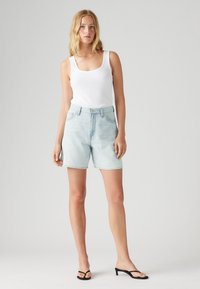 Ljusblå denimshorts med hög midja, utrustade med dragkedja och knappstängning samt sidofickor. En enkel vit linne kompletterar looken.