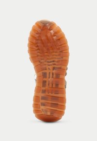 Kumisaappaan pohja oranssina, syvillä urilla ja tekstuuritiedoilla. Kestävä ja sopii erilaisille pinnoille tarjoamaan pitoa.