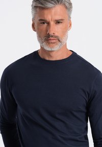 Merinovalkoinen pitkähihaisen crew neck-paita, joka on valmistettu teksturoidusta kankaasta. Paidan pinnassa on sileä pinta ja se on muotoiltu istuvasti, jossa on vain minimaalista ompelua.