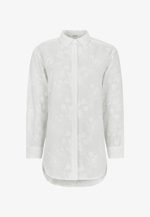 Ilgų rankovių balta marškinė su gėlių siuvinėjimu, apykakle ir mygtukų uždarymu. Turi išlenktą apačią ir tekstūruotą audinį.