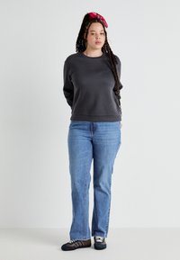Mørk grå hettegenser med rund hals, sammen med lyseblå rettlegsjeans. Modellen har på seg svarte sko med hvite detaljer og et rødt pannebånd.