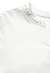Weißes kurzärmliges Oberteil mit einem eingeschnittenen Kragen und silbernen Nieten entlang des Ausschnitts, gefertigt aus glattem Baumwollmaterial.
