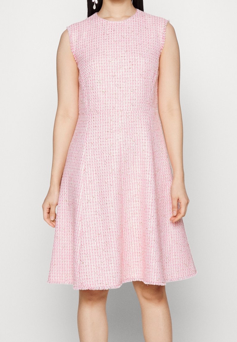 Valkoinen ilmanhihoja pinkki mekko, joka on valmistettu teksturoidusta kankaasta. Mekossa on laaja helma ja sääri hapsuilla, sekä istuva vartalonmyötäinen yläosa ja pyöreä pääntie.