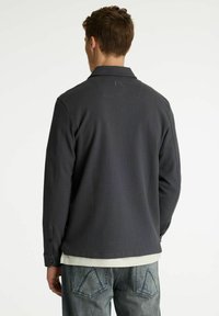 Graues Hemd mit Knopfleiste aus strukturiertem Stoff, gerippter Kragen und geradem Rückenteil. Kombiniert mit hellblauen Denim-Jeans mit Taschen-Details.