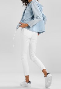 Light blue denim jacket with a hood, white fitted trousers, and white sneakers with navy accents, creating a casual layered look.