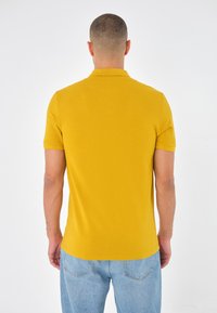 Polo à manches courtes en coton jaune vif, avec un col classique et une coupe ajustée, porté avec un jean en denim bleu clair.