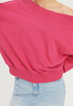 Suéter rosa sin hombros combinado con jeans de talle alto en azul claro, usado por una persona contra un fondo sencillo.