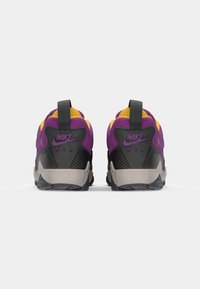 Nike Air tenisice s pogledom straga. Gornji dio u ljubičastoj i žutoj boji, crni akcenti, strukturirani petni dio i siva potplata s uzorkom za prianjanje.