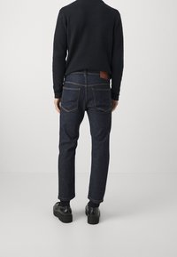 Tummansiniset suoralahkeiset farkut, joissa on kullanväriset saumat, takayoke ja kaksi takataskua. Yhdistetty mustaan teksturoidun neulepuseron kanssa.