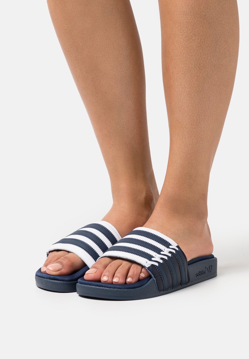 Navy blue slide sandals with white striped straps, a flat design, and textured footbed for grip, featuring subtle branding on the side.