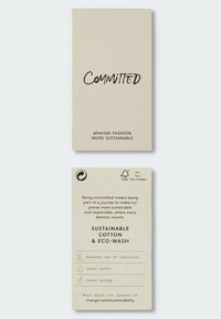 Kestävä muoti -etiketti vaaleanruskeassa kierrätetyssä pahvissa, jossa on mustalla korostettu "Sitoumus" ja ekopesuominaisuudet.
