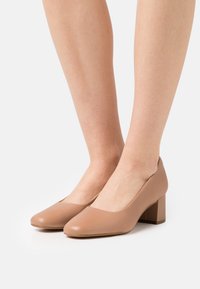 Beige kožené lodičky na vysokém podpatku s kulatou špičkou a hladkým povrchem. Blokový podpatek je krátký a robustní, což zajišťuje stabilitu.