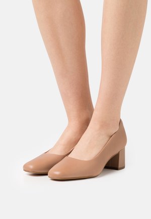 Zapatos de tacón alto de cuero beige con puntera redondeada y superficie lisa. El tacón cuadrado es corto y robusto, proporcionando estabilidad.