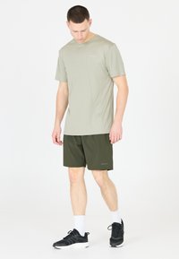 Licht olijfgroen t-shirt met korte mouwen, gecombineerd met donkergroene shorts. Zwarte sportschoenen met witte sokken. Eenvoudig, functioneel ontwerp.