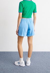 Green and blue ribbed short-sleeve shirt, light blue shorts with elastic waistband, white sneakers with blue accents, plain background.