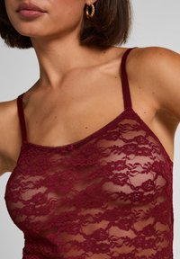 Μπορντό κορυφή δαντέλας με λεπτές τιράντες, με σχέδιο λουλουδιών και μικρή διακόσμηση τριαντάφυλλου μπροστά, ημιδιάφανη υφή.