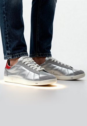 Sneakers argento con accenti in suede grigio, dettaglio rosso sul tallone e lacci bianchi. Suola illuminata notevole e superficie testurizzata. Design classico.