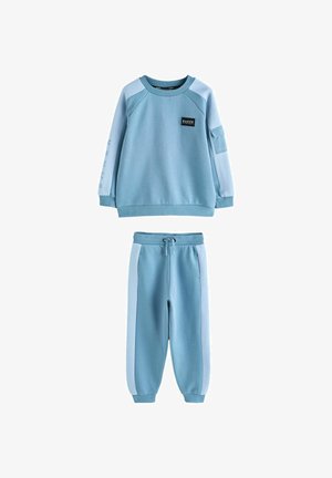 Jasnoniebieska bluza i dopasowane dresy wykonane z miękkiej tkaniny z prążkowanym kołnierzem, zdobione białymi akcentami oraz naszywką z logo na piersi.