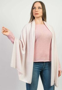 Lys rosa sjal lavet af blødt stof, der faldet glat over en lys rosa top. Modellen bærer blå jeans og holder sjalet med den ene hånd.