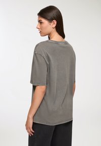 T-shirt grigio a maniche corte in cotone lavato con vestibilità rilassata, scollo rotondo e dettagli di cucitura visibili lungo le maniche e l'orlo.