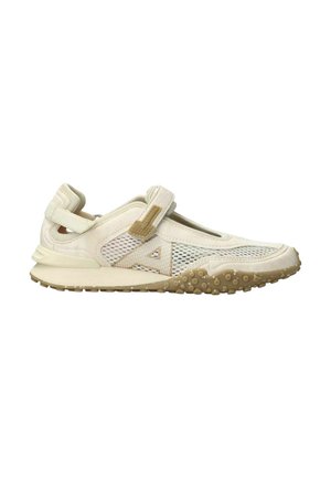 Chaussure de sport beige clair avec des panneaux en mesh, une sangle ajustable, une semelle texturée et des points de grip en caoutchouc beige sur la semelle extérieure.