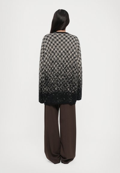 Oversized black and beige knit sweater with a diamond pattern, fading from light to dark. Paired with loose brown wide-leg trousers.