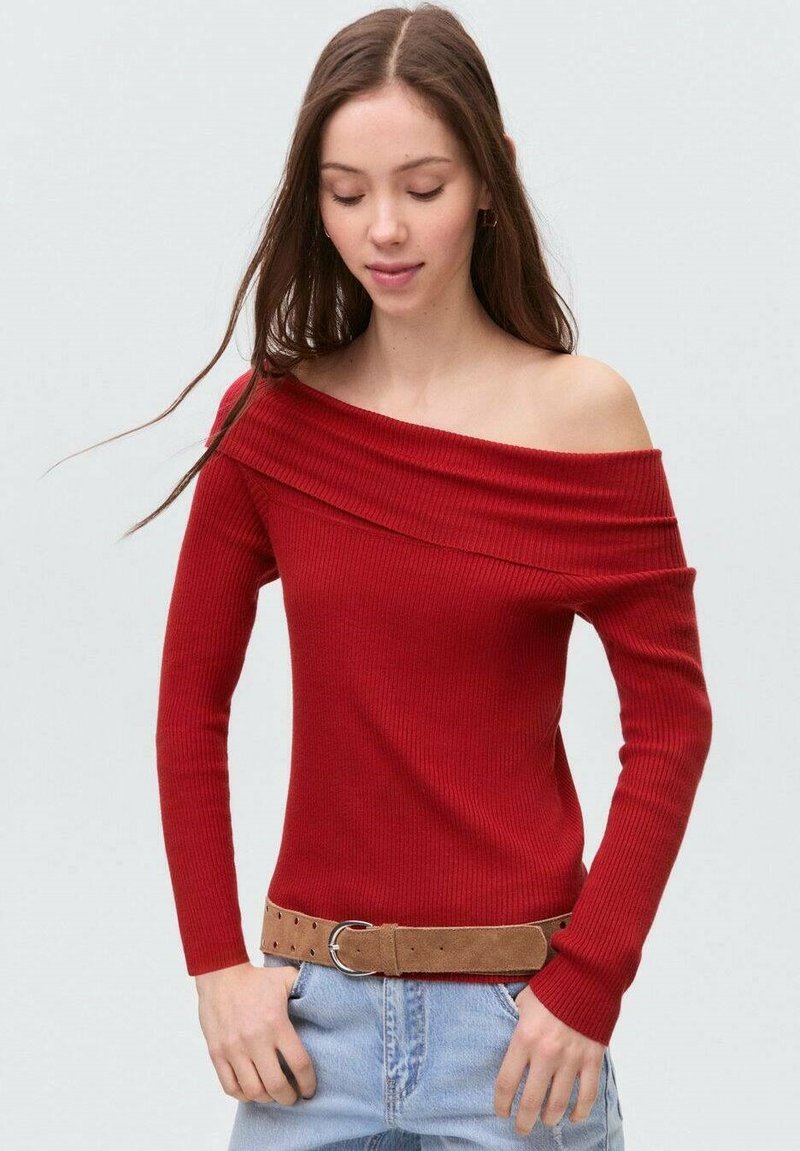 Röd ribbad off-shoulder topp med långa ärmar, med en bred halsringning. Kombinerad med en ljusblå denimskjorta med knappar och ett beige bälte.