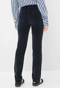 Marineblauwe corduroy broek met een rechte pijp; beschikt over twee achterzakken en een zachte, gestructureerde stof. Gecombineerd met zwarte sandalen.