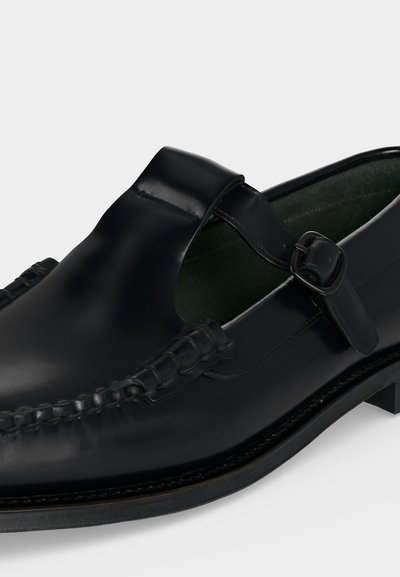 Chaussure habillée en cuir noir avec bride à boucle et détails tissés sur l'avant arrondi, talon bas et finition lisse.