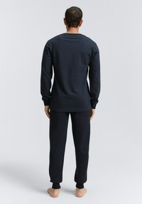 Navyblaues Langarmoberteil und passende Hose, aus strukturiertem Stoff. Das Oberteil hat einen runden Ausschnitt, während die Hose eng anliegenden Knöchelabschluss hat.