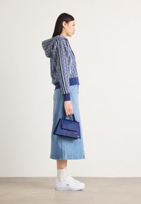 Hanorac cu model marin cu dungi albe, fustă lungă din denim deschis, adidași albi și o geantă mică albastră cu mâner.