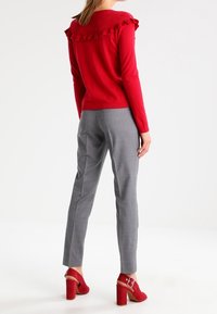 Rode trui met gerimpelde halslijn, grijze op maat gemaakte broek en rode blokhak schoenen met enkelbandje. Overal een gladde textuur.