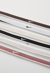 Nike gumičky na vlasy v piatich farbách: tmavohnedá, čierna, biela, ružová a svetlo ružová. Každá má na jednej strane kontrastné čierne logo Nike.