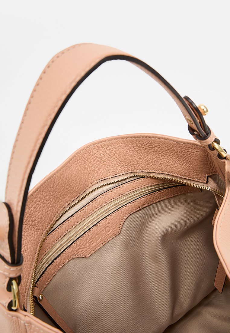 Innenseite einer handgefertigten tanfarbenen Lederhandtasche mit beigem Futter, zwei Reißverschluss-Fächern und braunen Akzenten am Tragegurt und den Reißverschlusskanten.