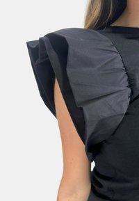 Top nero con maniche voluminose a balze realizzate in un tessuto testurizzato, che mette in risalto un corpo aderente e una silhouette pulita.