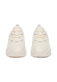 Zapatillas de color marfil con un upper de tela texturizada, puntera reforzada, suela de goma gruesa y cordones en la parte frontal para un ajuste seguro.