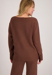 Bruine gebreide trui met een losse pasvorm, geribbelde manchetten en een brede halslijn. Zachte textuur, gecombineerd met bijpassende bruine broek.